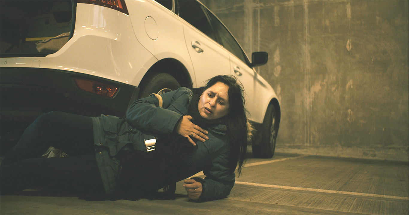 Woman on floor in car park, clutching chest.