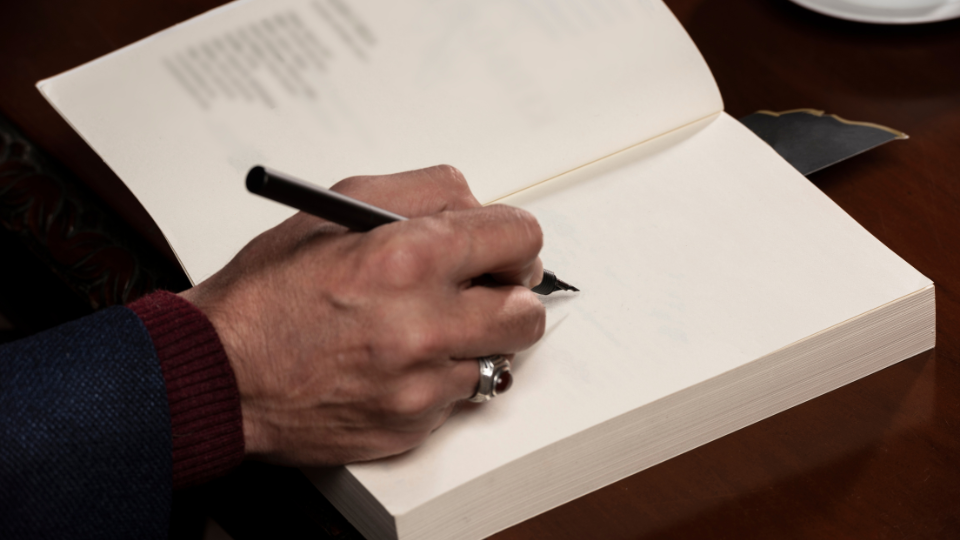 Author's hand, holding pen and signing book