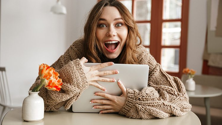 Good UX makes learning enjoyable and increases engagement, comprehension, and retention. A woman in a sweater hugs her laptop with a joyous expression.