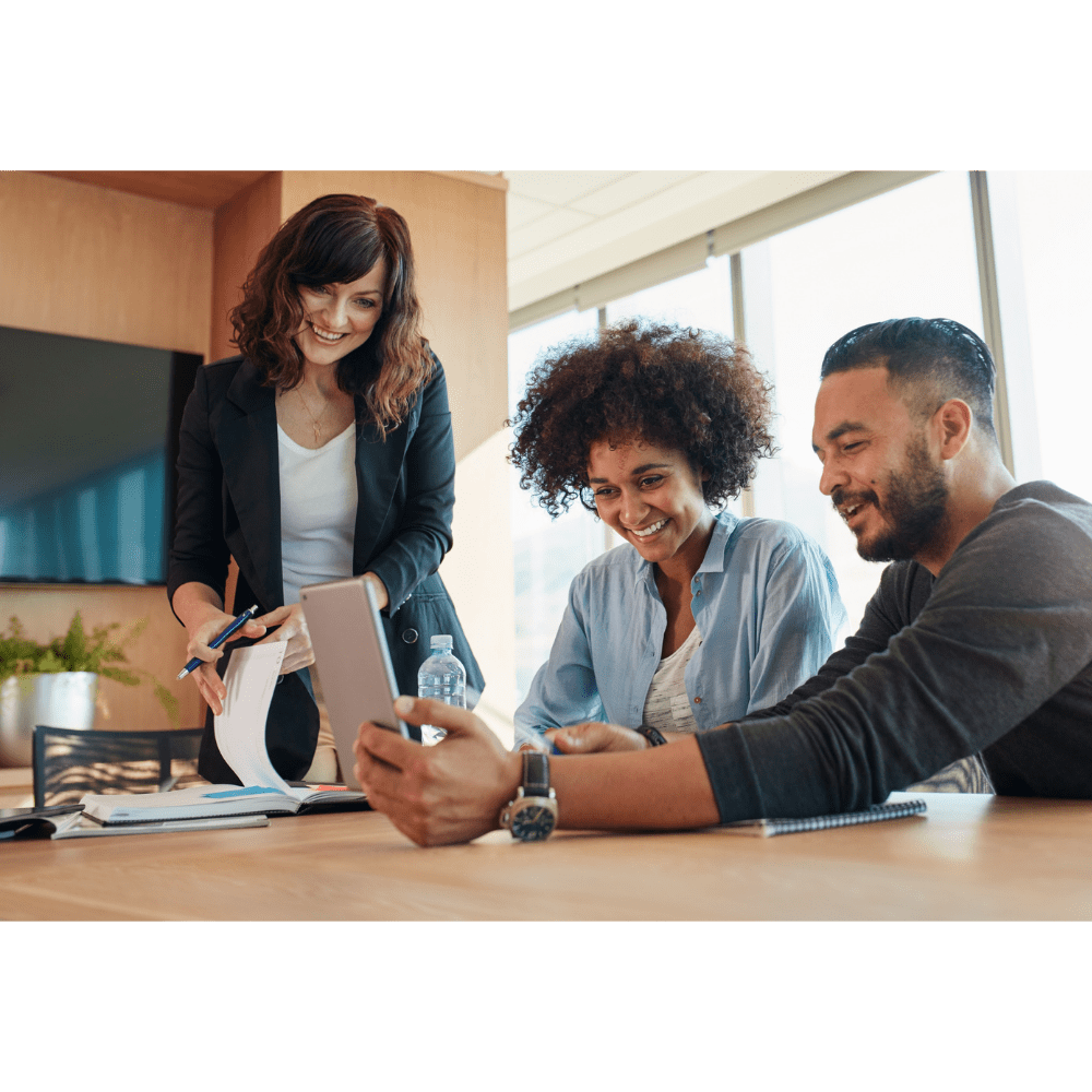 Smiling team looking at laptop in sunny, modern conference room