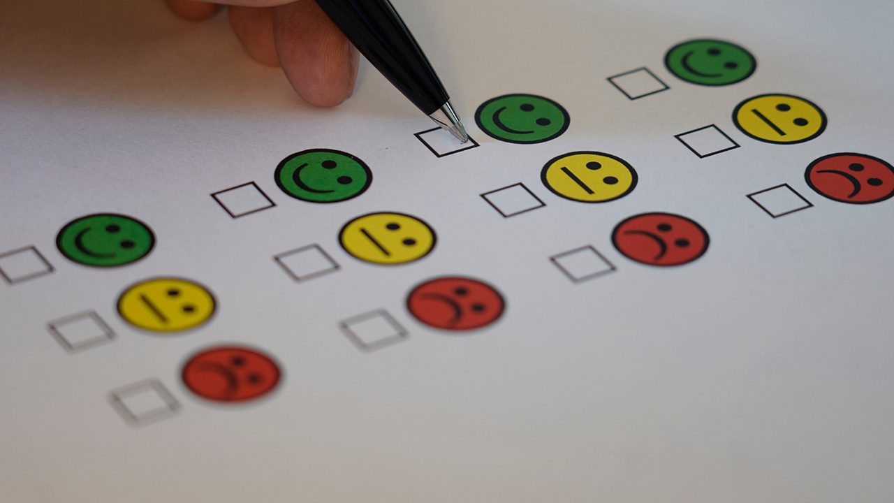 Close up of smiling face rating system - happy, neutral, sad/angry - with a person holding a pen about to tick the happy face.
