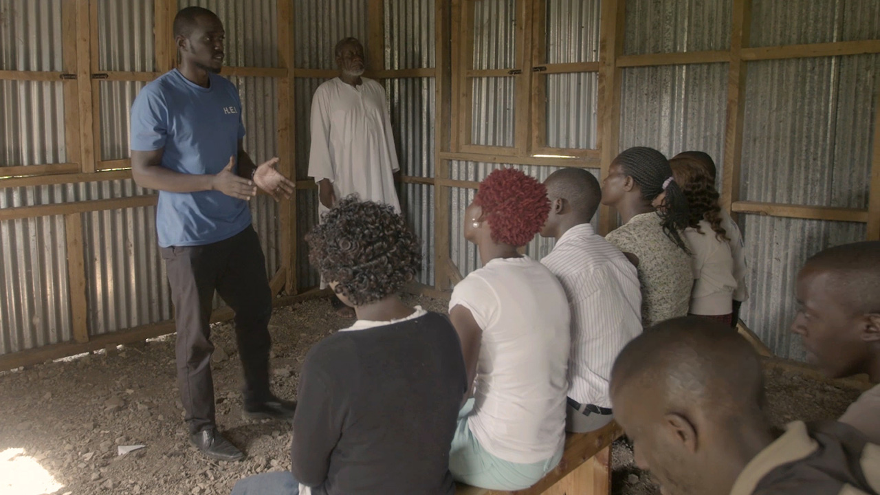 Still from Field Security Management course shows a local aid worker speaking in front of a seated crowd.